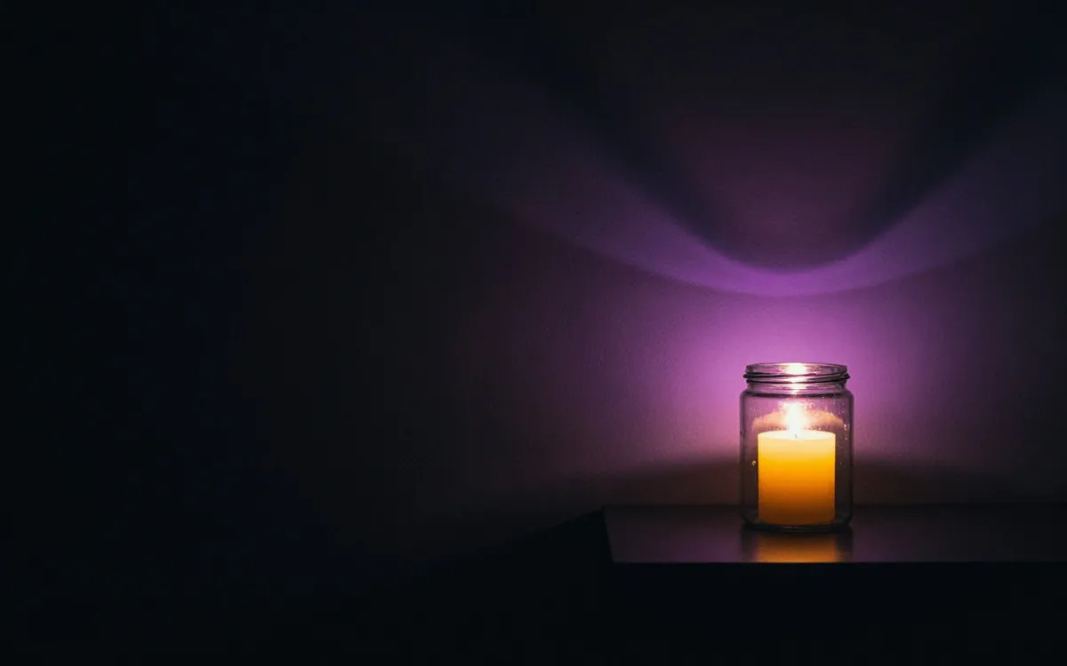 Glass jar with a small lit candle on a dark shelf