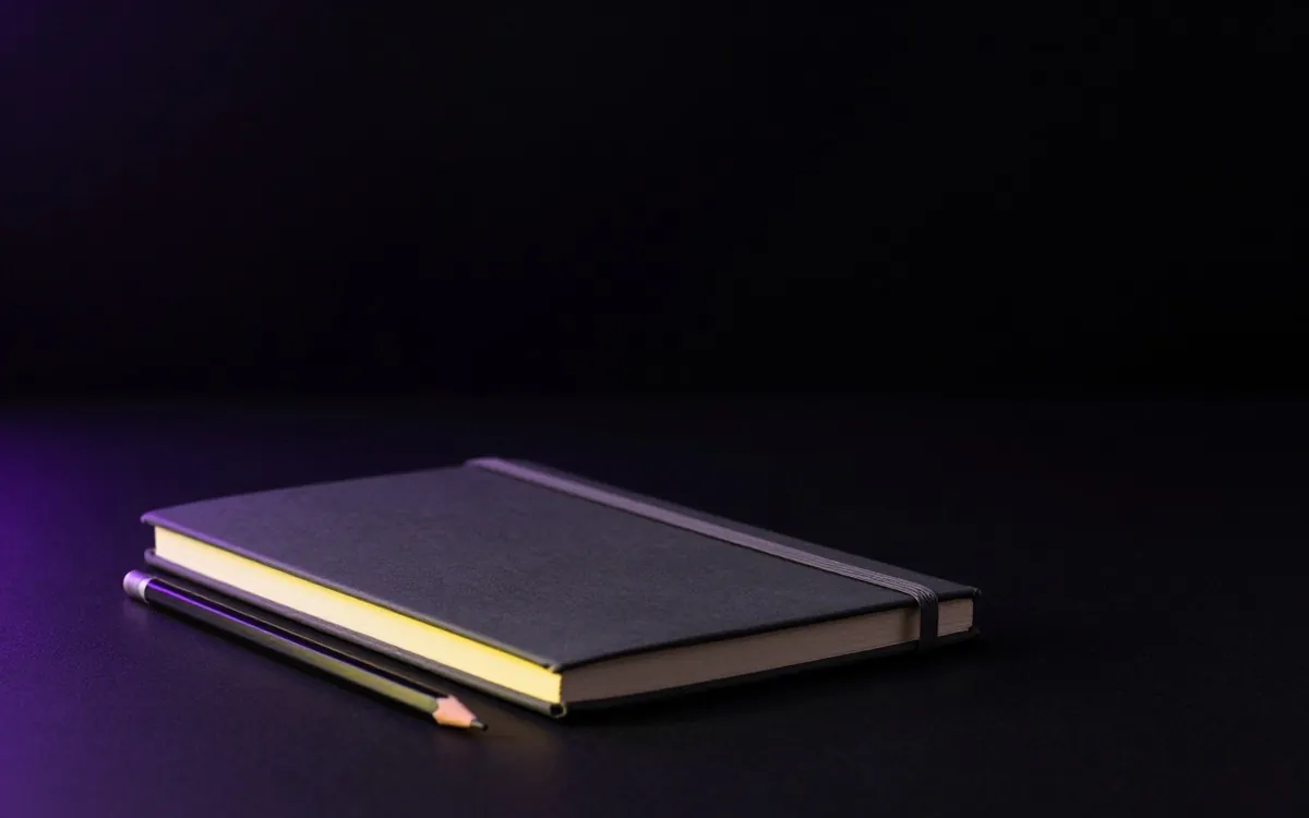 Closed notebook and pencil on a dark surface