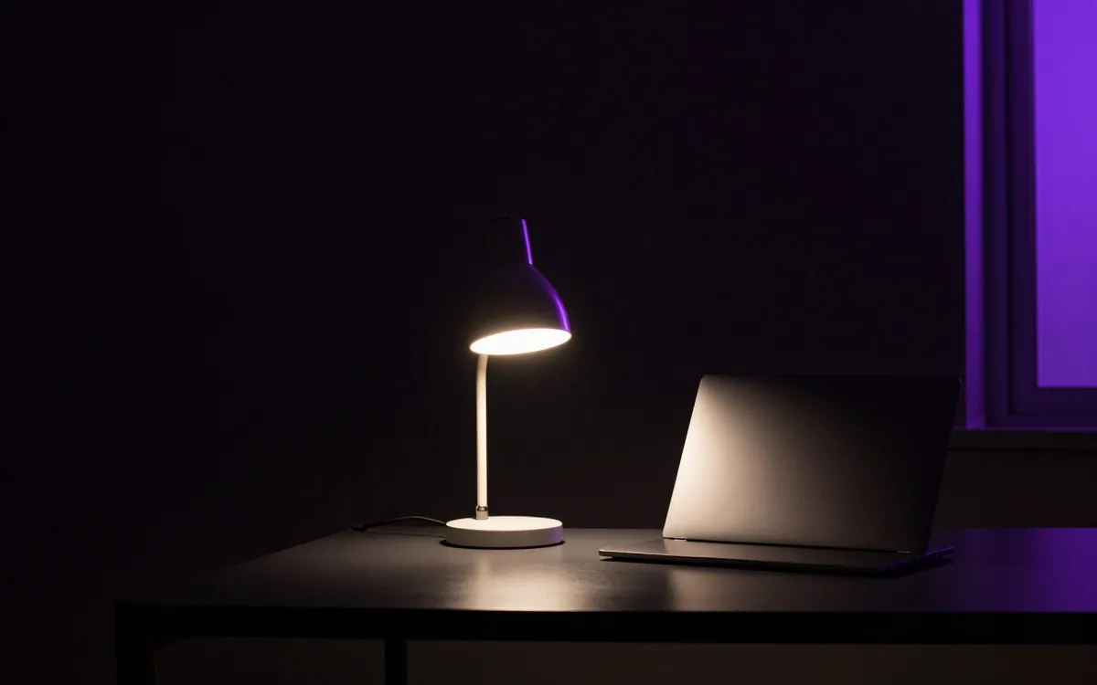 Desk lamp on over an empty dark desk with a closed laptop